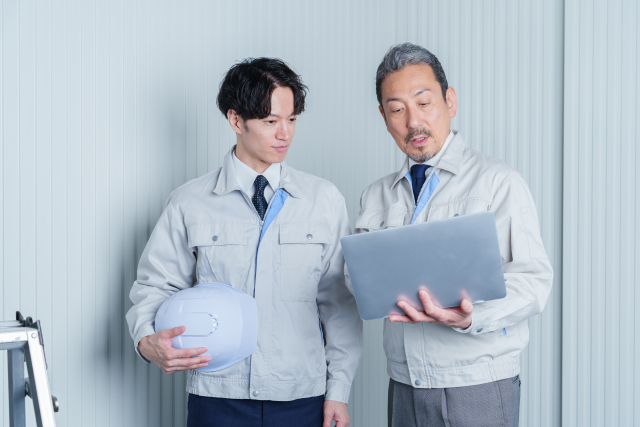 ノートパソコンを見ながら打ち合わせをする作業服姿のスタッフ